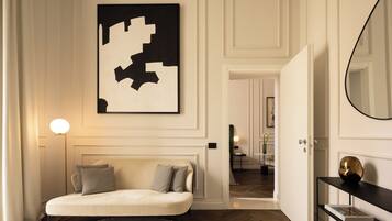 A modern interior with a sofa, a large abstract painting, a round mirror, and a hallway leading to another room.