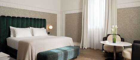 A hotel room with a bed, a bedside table, a round table with chairs, and a bench.