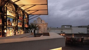A bar area with shelves of bottles, a seating area with chairs, and a view of a historic building. - Patria Palace Hotel Lecce - Leading Hotels of the World (Lecce)