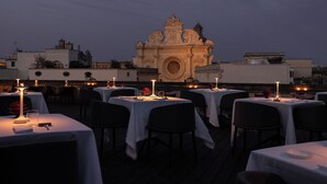 A rooftop dining area with tables set for guests, a large ornate building in the background, and a clear sky. - Patria Palace Hotel Lecce - Leading Hotels of the World (Lecce)