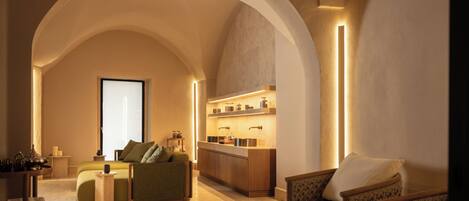A modern interior with a sofa, armchair, and kitchen area under a large arched ceiling.