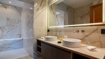 A modern bathroom with a marble vanity, two sinks, a large mirror, and a walk-in shower.