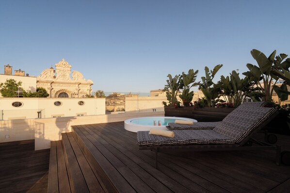 Une terrasse sur le toit avec une piscine, des chaises longues et une vue sur un bâtiment historique.