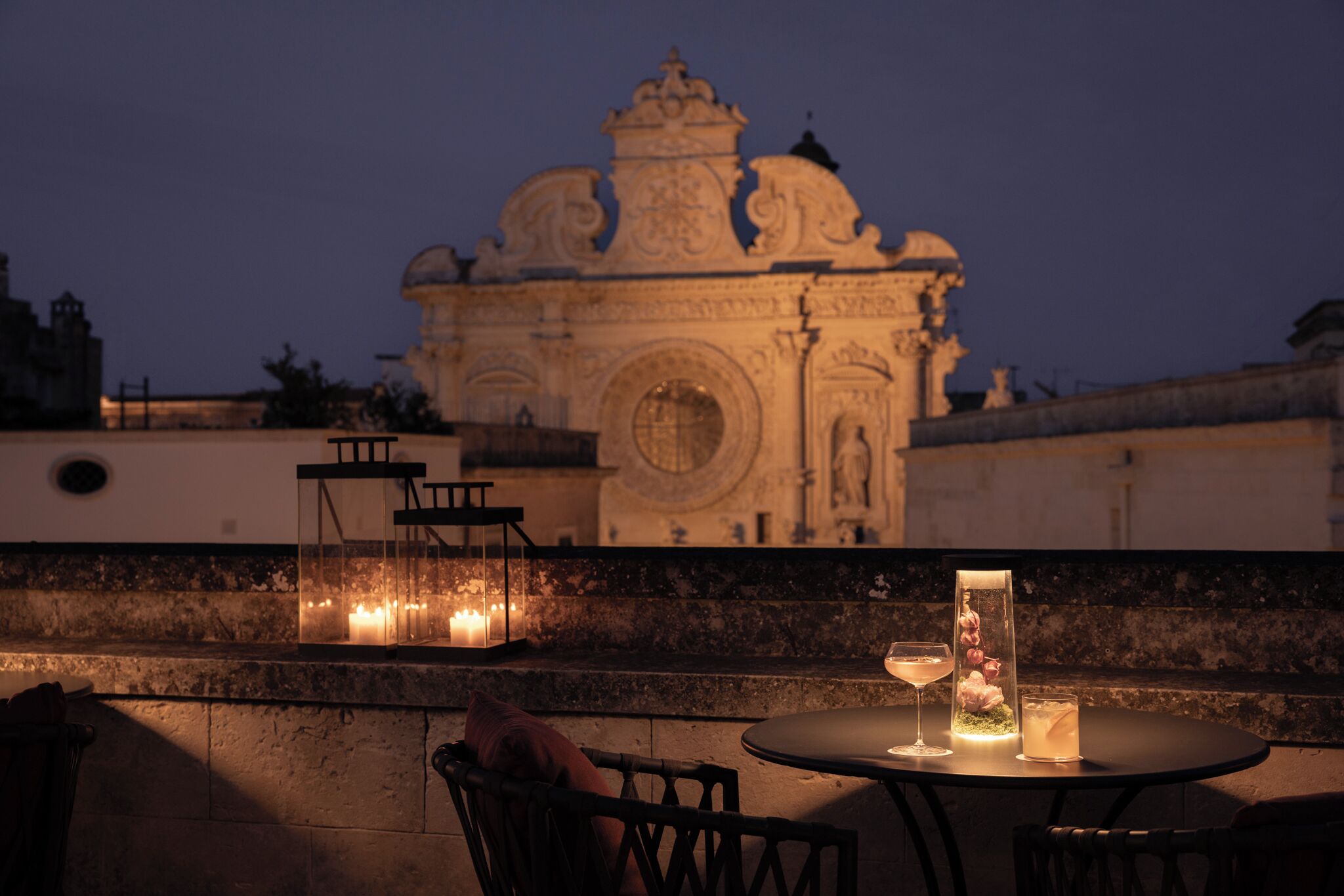 Uma área de refeições ao ar livre com mesa, cadeiras, velas e um centro de mesa decorativo.