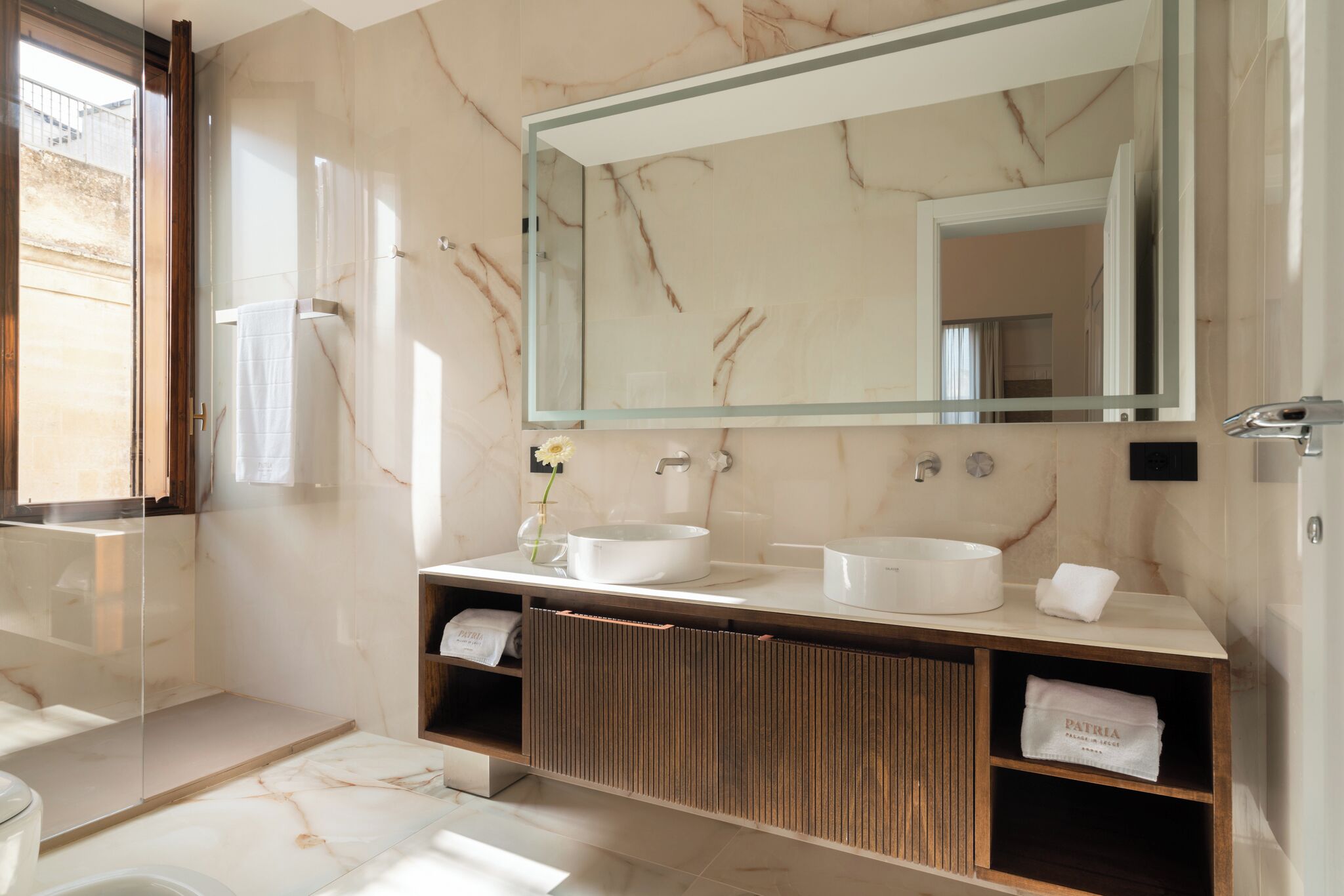A modern bathroom with a large mirror, two sinks, a wooden vanity, and a towel rack.