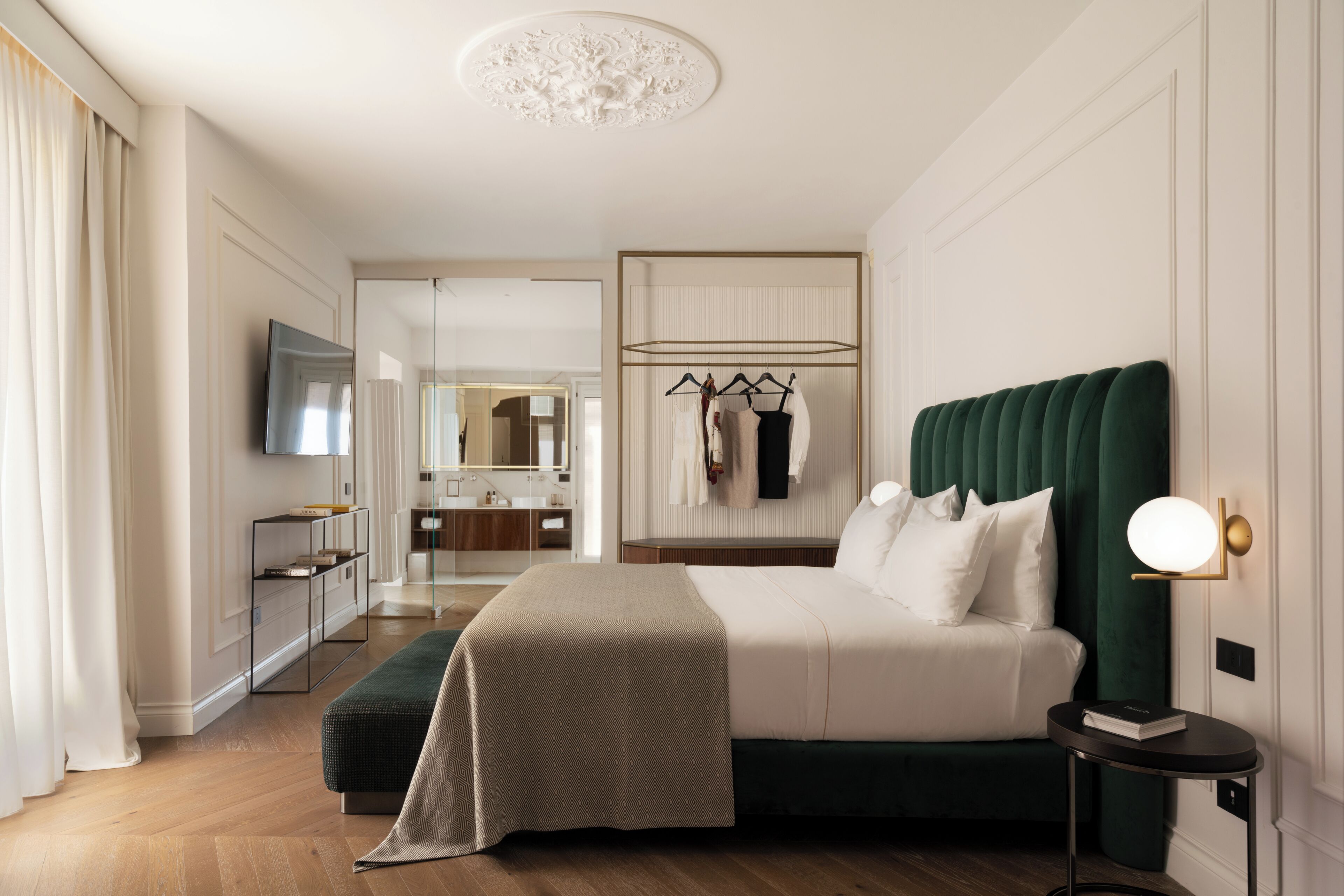 Habitación de hotel con una cama grande, una mesita de noche, un televisor, un armario y un baño visible a través de una puerta abierta.