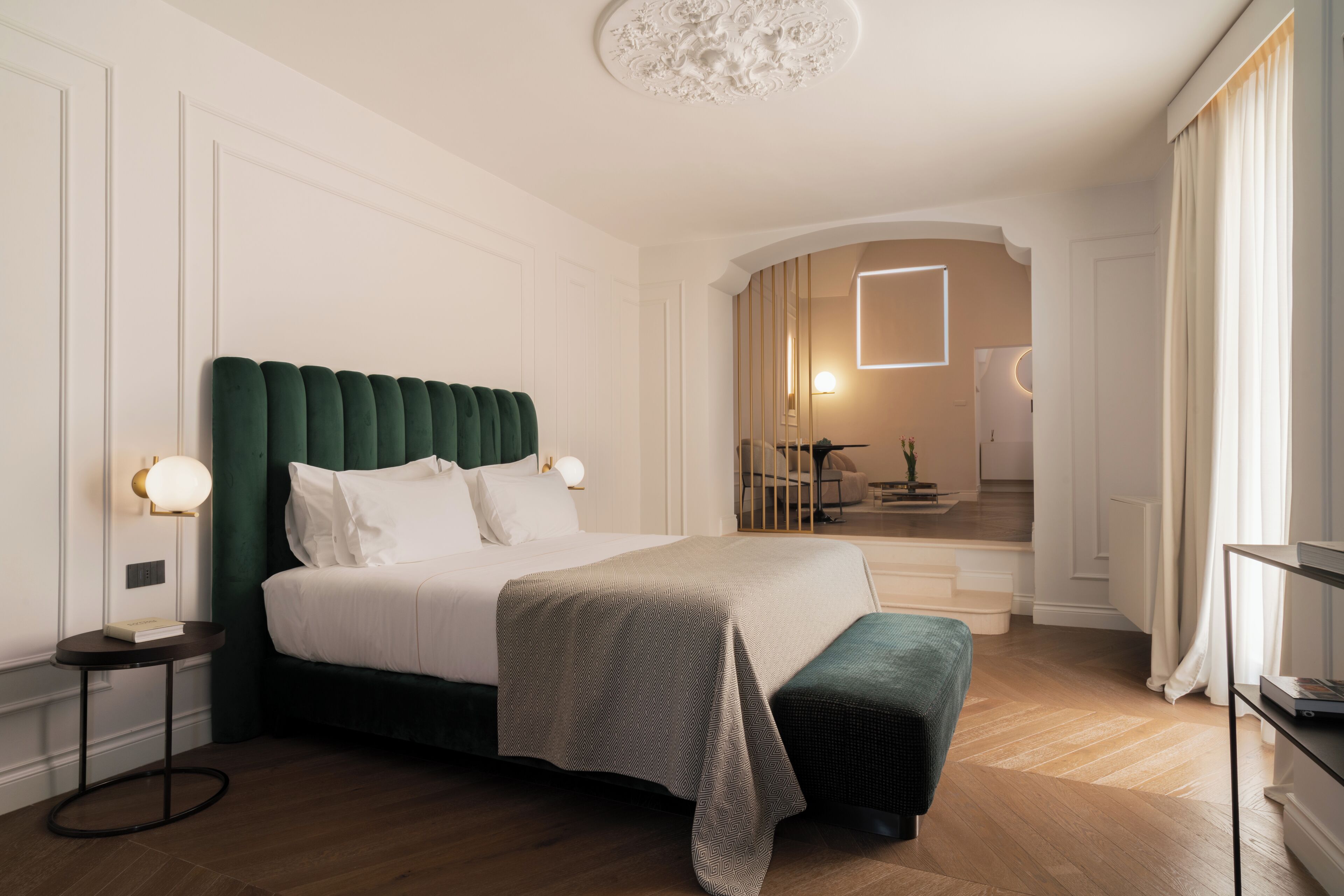 A hotel room with a large bed, a bedside table, a lamp, and a view of the hallway and staircase.