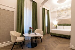 Una habitación de hotel con una cama, dos sillas, una mesa redonda y un florero con flores.