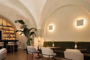 A bar area with shelves of bottles, a seating area with a green sofa and round tables, and a large plant.