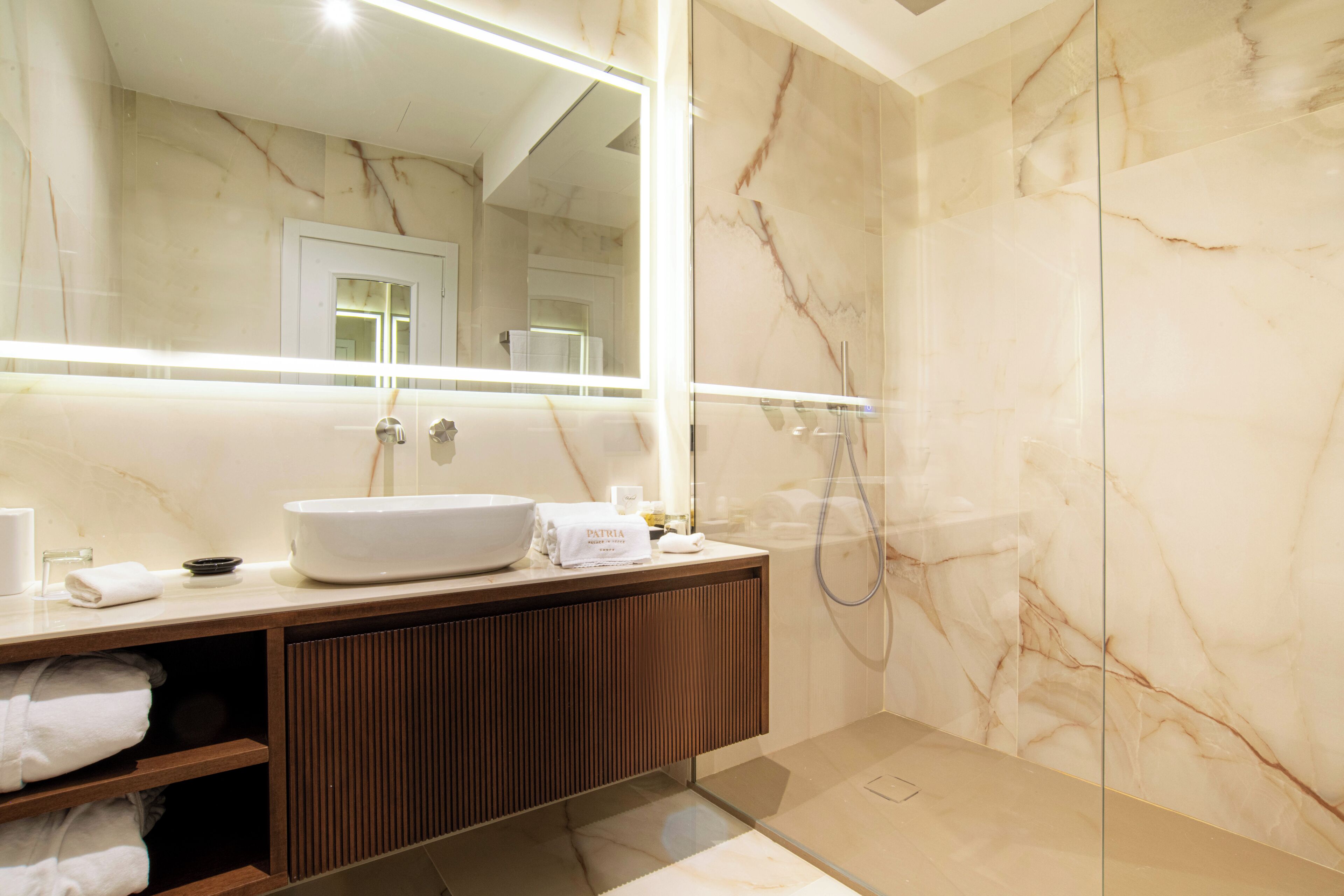 Een moderne badkamer met een marmeren wand, een grote spiegel, een wastafel en een douche.