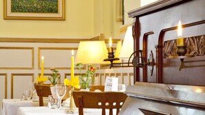 A dining area with a piano, tables set with white tablecloths, candles, and a painting on the wall. - Hotel Westend (Merano)