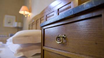 Een houten dressoir met een messing handvat, een bed met witte lakens en een wandlamp.