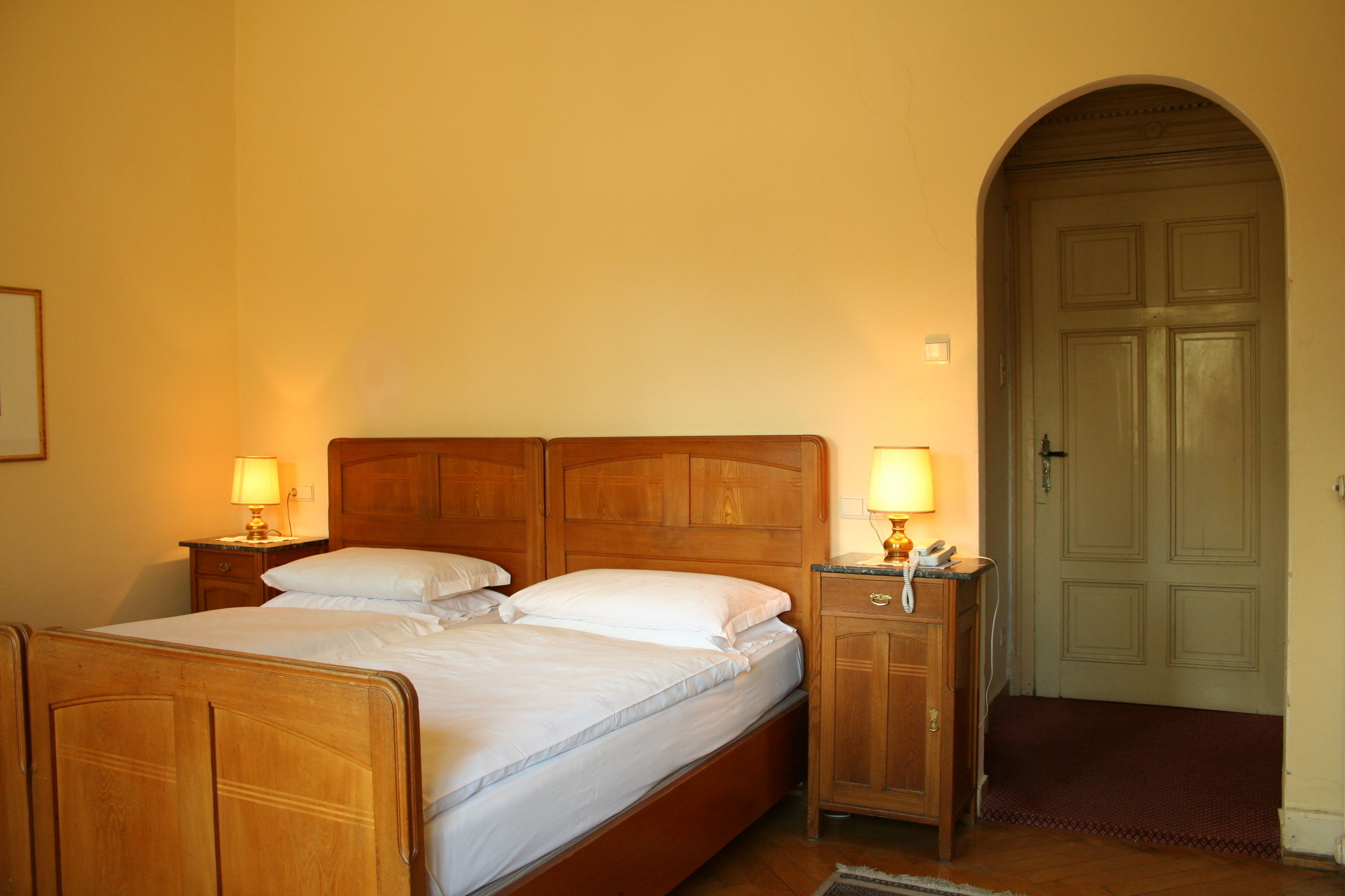 Un dormitorio con una cama de madera, dos mesitas de noche con lámparas, un armario de madera y una puerta con arco.