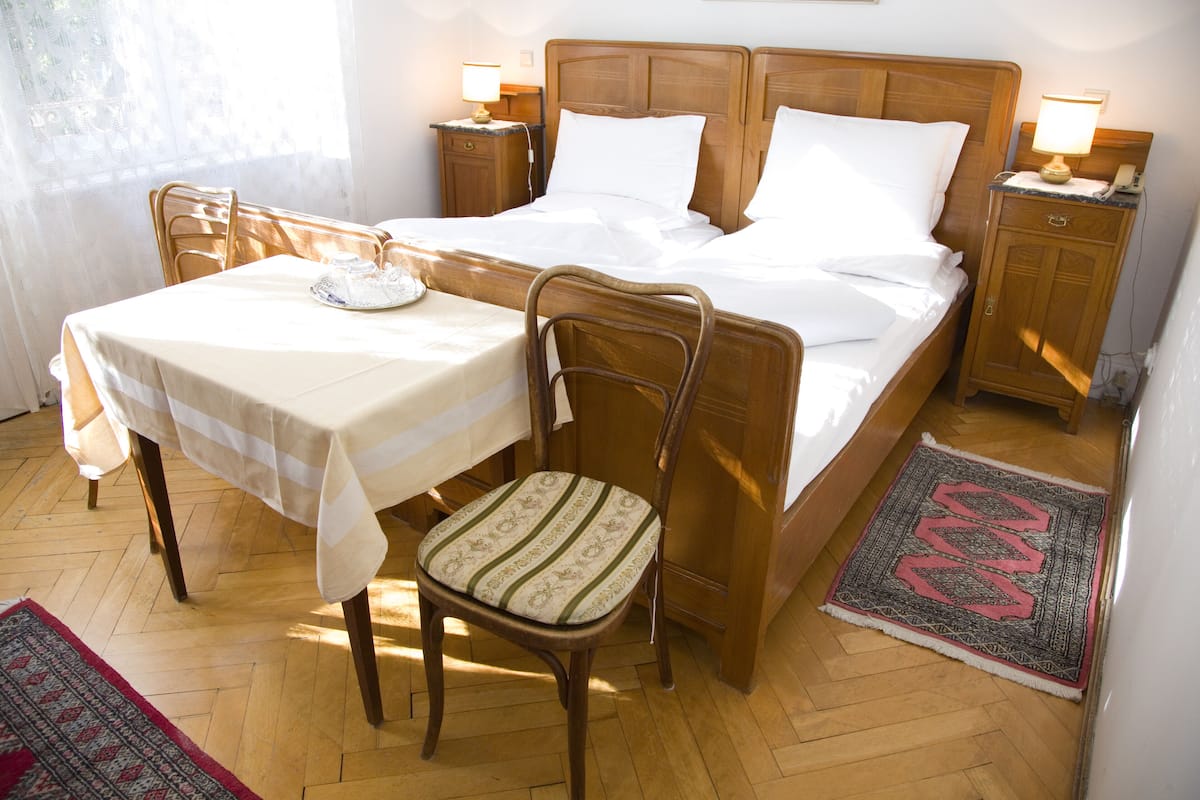 A neatly arranged bedroom with a wooden bed, a bedside table, a chair, and a small table.