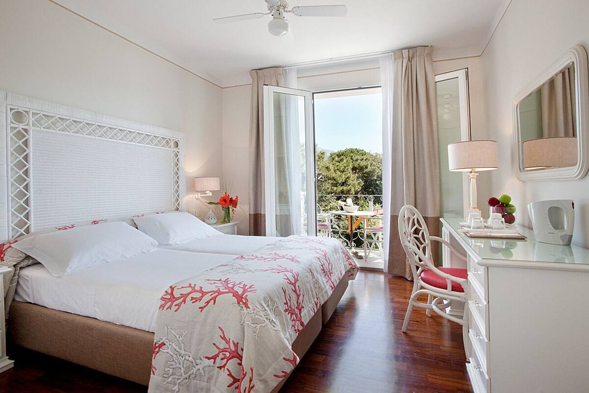 A hotel room with a bed, a desk, a chair, and a balcony with a table and chairs.