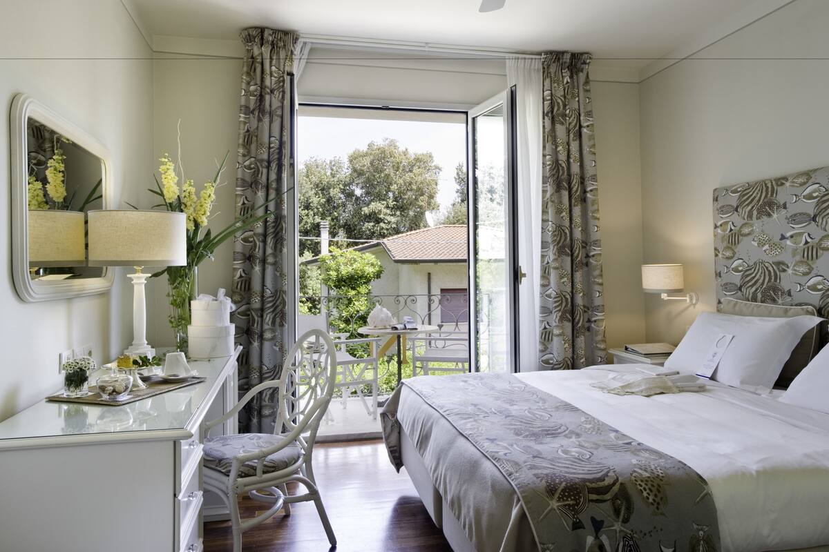 A hotel room with a bed, a desk, a chair, a table, and a balcony with a view of the outside.