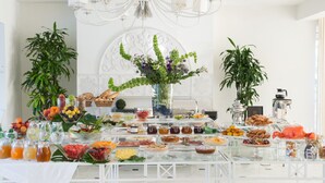 A buffet setup with various food items and beverages, a decorative vase, and potted plants. - Hotel Il Negresco (Forte dei Marmi)