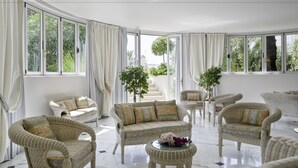 A spacious room with wicker furniture, large windows, and a view of greenery outside. - Hotel Il Negresco (Forte dei Marmi)