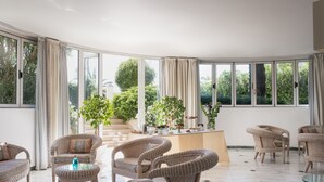 A spacious room with large windows, wicker furniture, and a central table with potted plants. - Hotel Il Negresco (Forte dei Marmi)