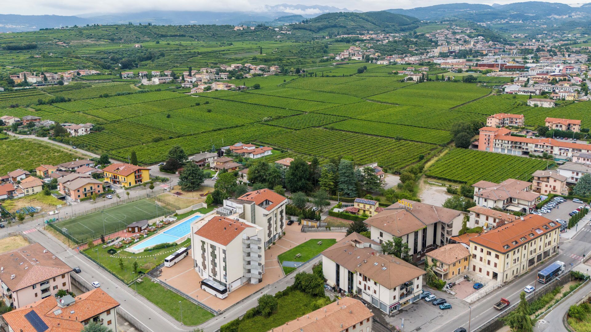 A hotel with a swimming pool, surrounded by green fields and residential buildings.