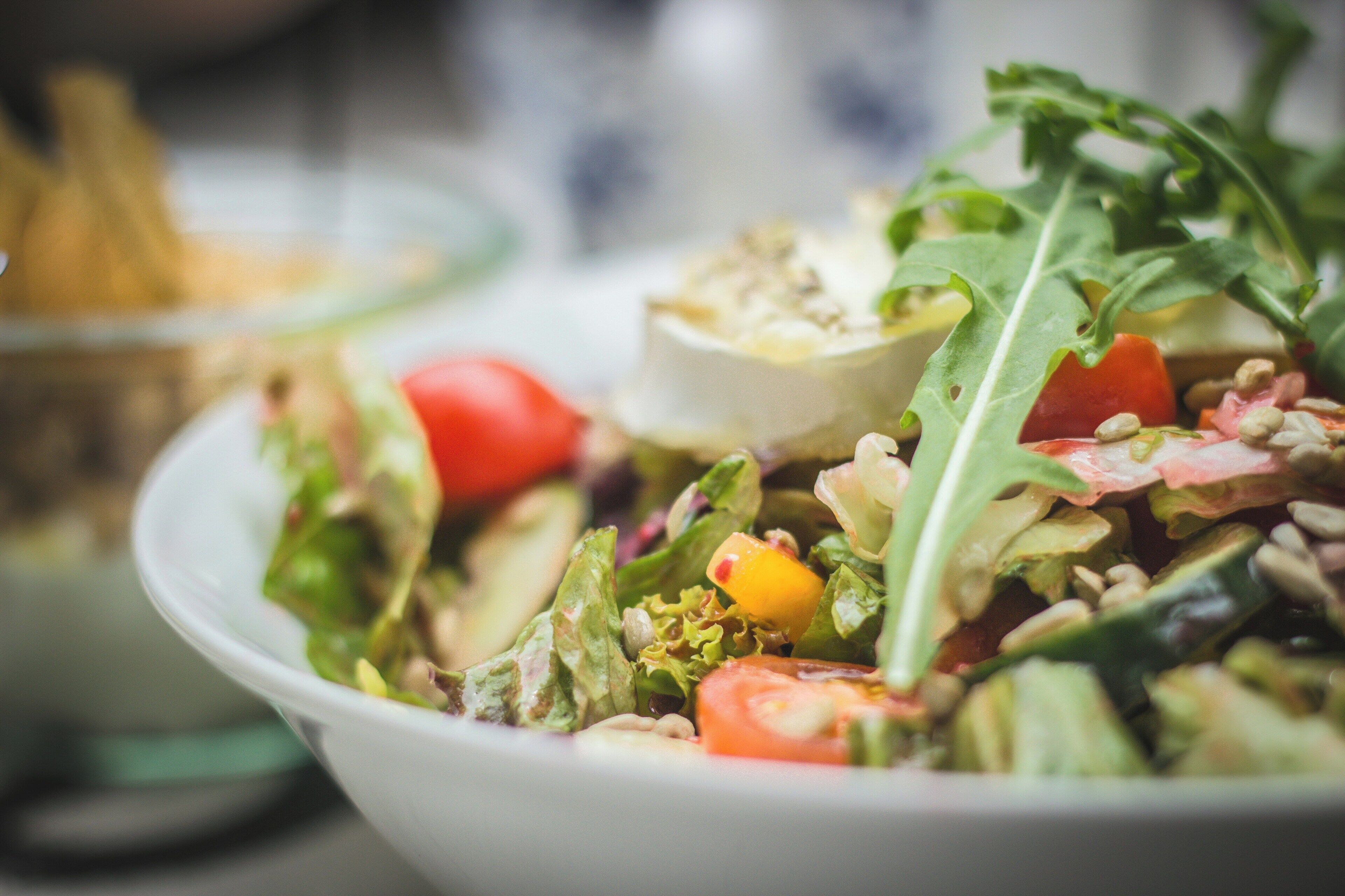 A bowl of salad with various vegetables and a piece of cheese.