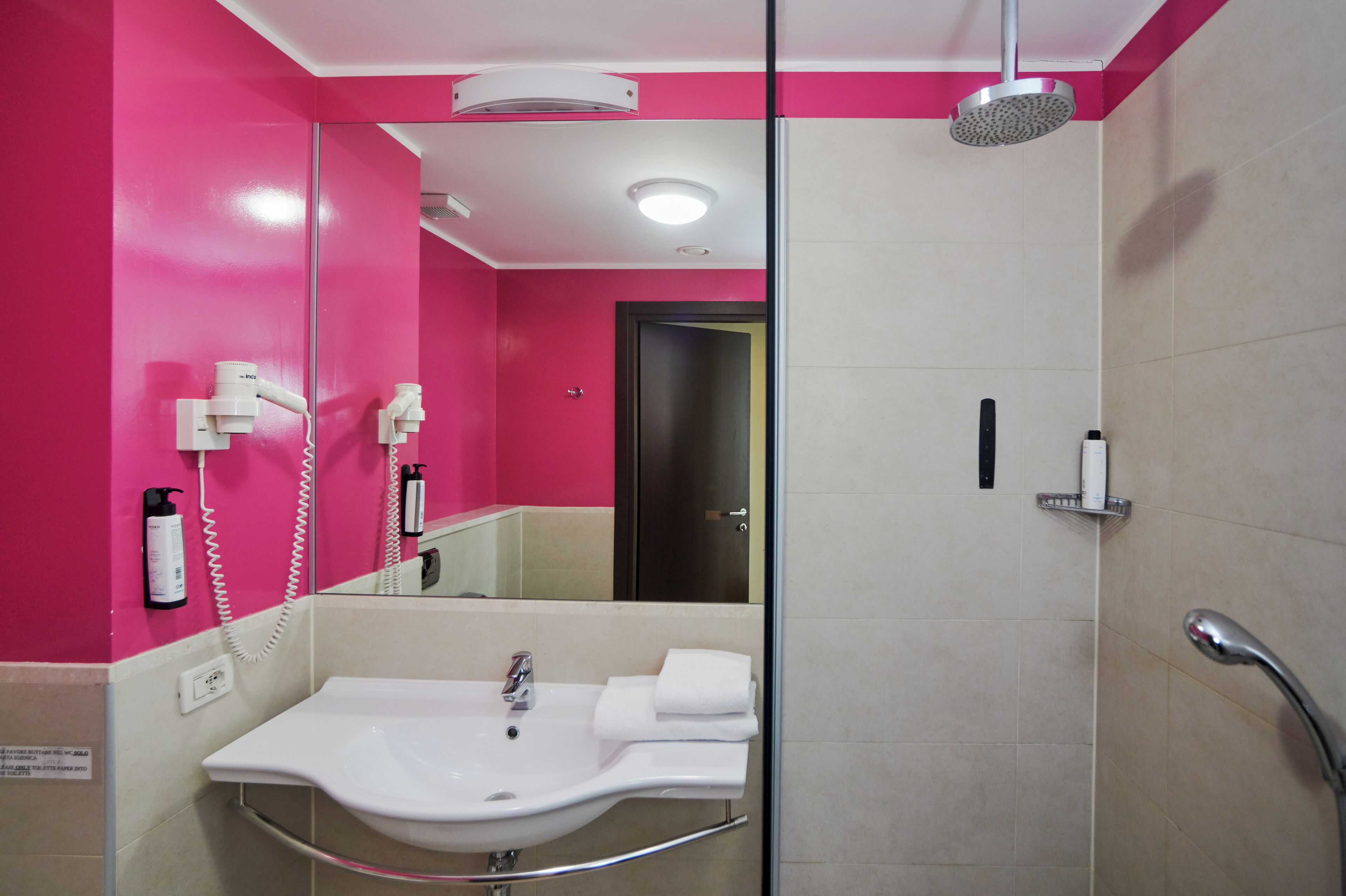 A modern bathroom with a pink wall, a white sink, a mirror, a shower, and a towel rack.