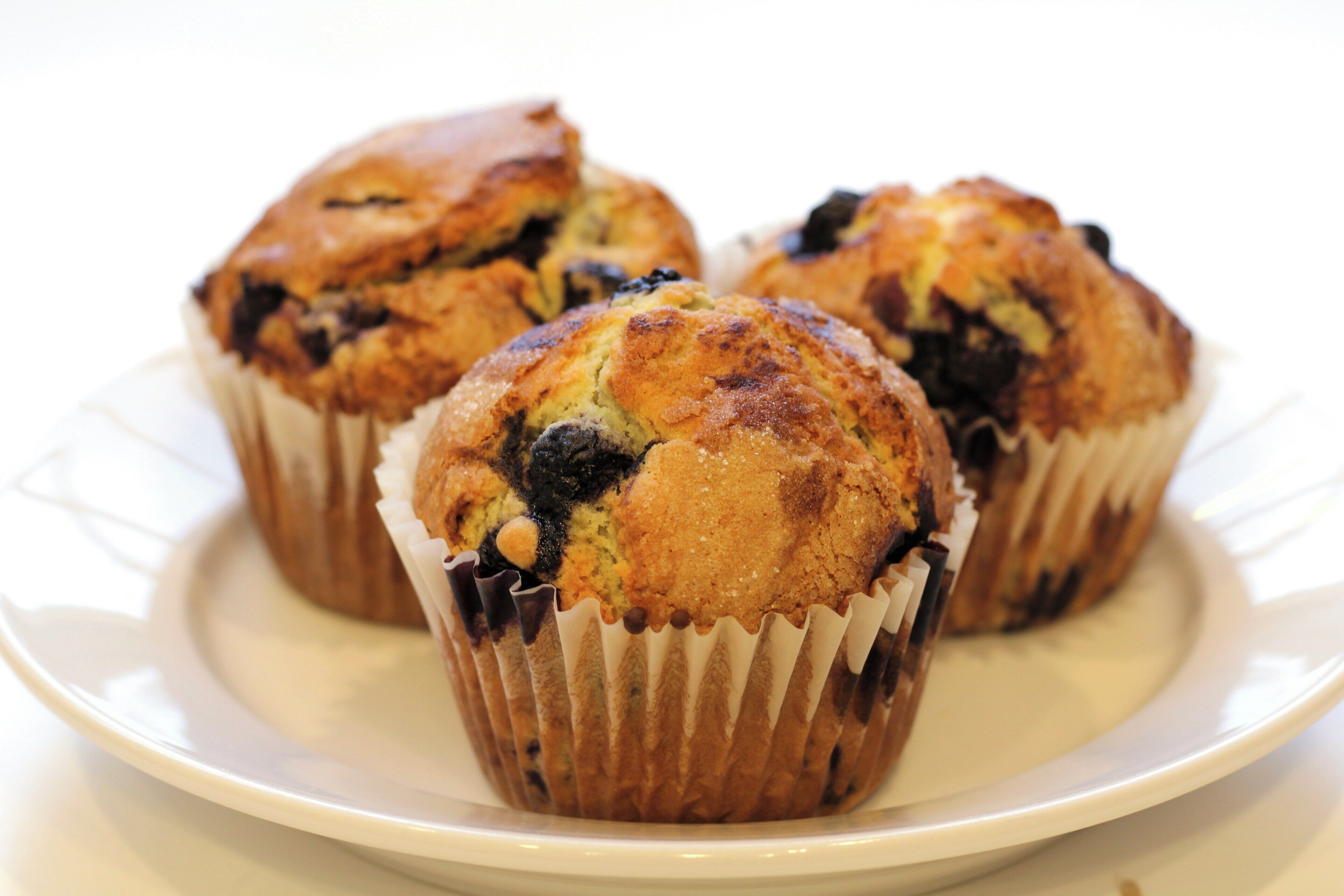Three muffins in paper cups on a white plate.