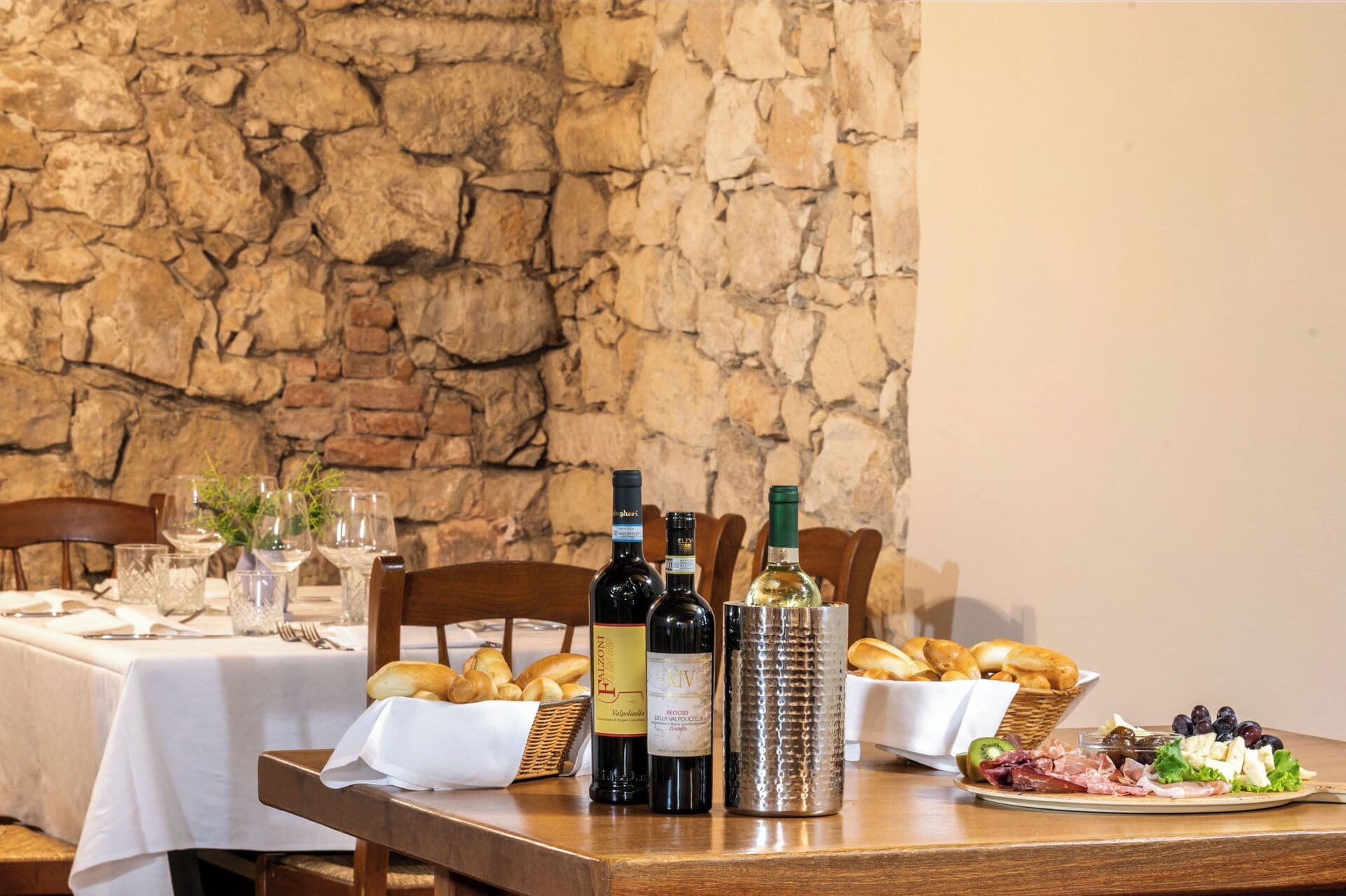Une table à manger dressée avec des bouteilles de vin, du pain et une planche de charcuterie.
