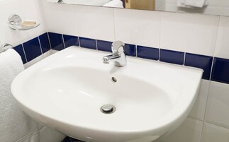 Un lavamanos blanco con grifo de cromo, un espejo encima y paredes con azulejos azules.