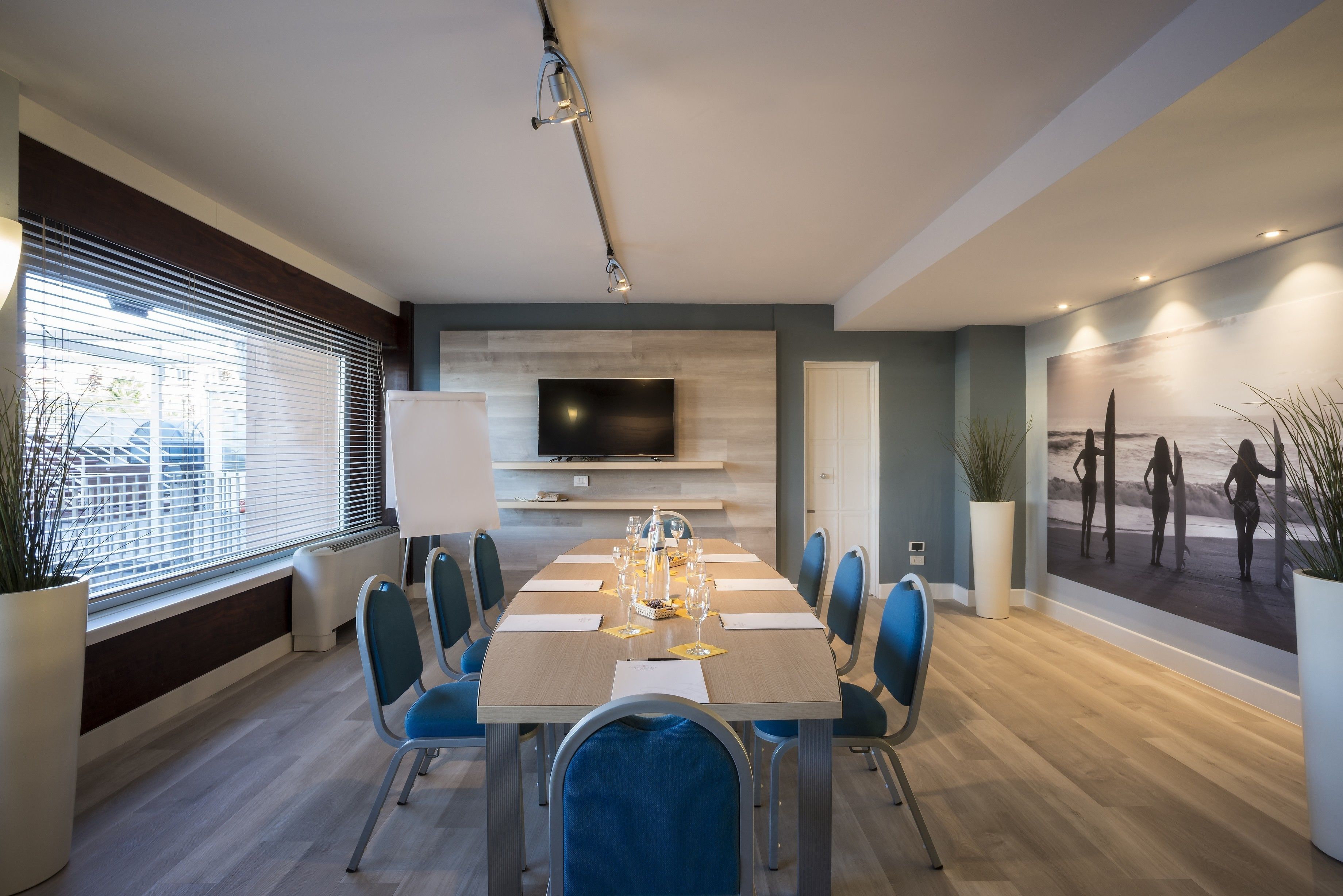 A modern dining area with a long table, blue chairs, and a flat-screen TV on the wall.
