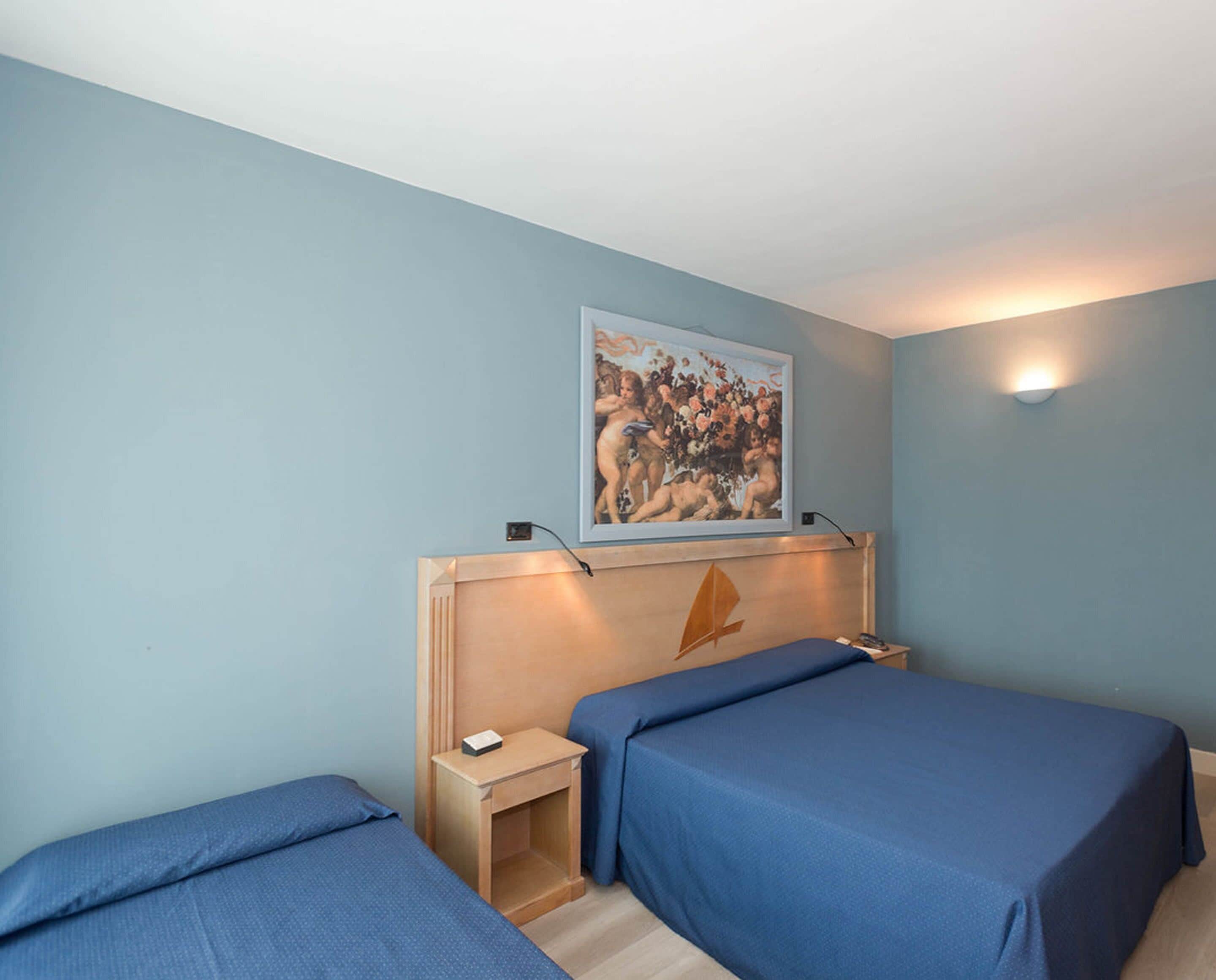 Une chambre d’hôtel avec deux lits simples, une tête de lit en bois, une table de chevet et une œuvre d’art encadrée au-dessus de la tête de lit, ainsi qu’un luminaire fixé au mur.