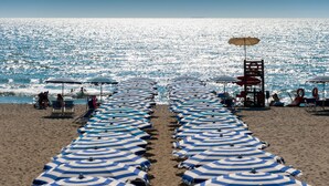 Una playa con hileras de sombrillas y sillas de playa a rayas azules y blancas.
