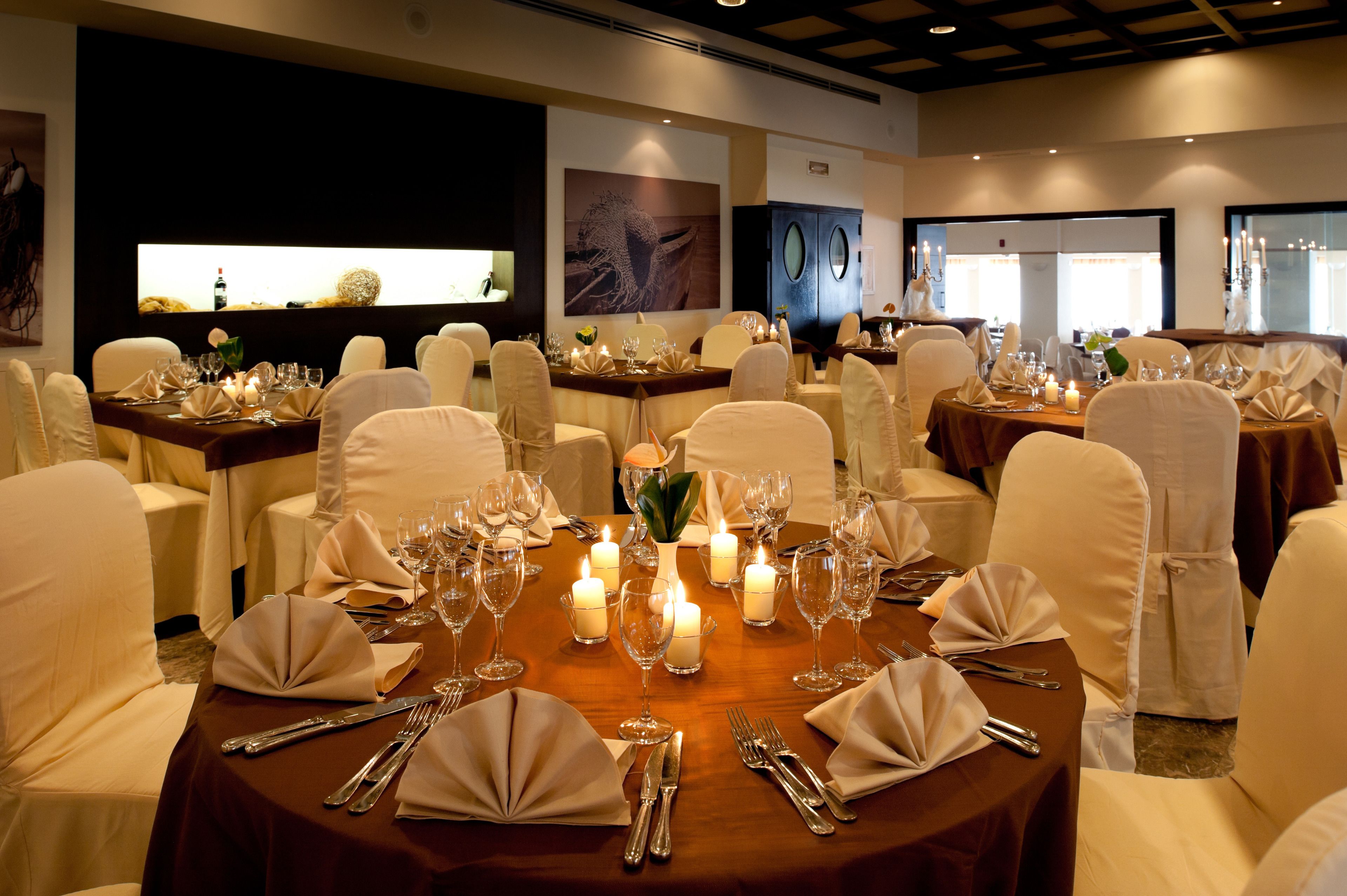 Une salle à manger élégante, avec des tables rondes disposées pour accueillir plusieurs convives, chaque table étant agrémentée de bougies et de serviettes blanches.