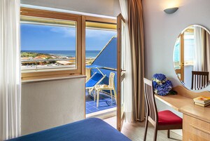 Una habitación con cama, un escritorio con silla, un espejo y vista a la playa y al océano a través de una ventana.