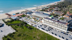 Vista aérea de un hotel costero con varias edificaciones, un estacionamiento y una playa al fondo.