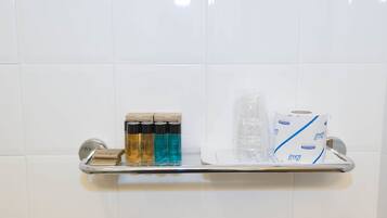 Ein Badezimmerschrank mit Seifenspendern, einem Glasbehälter und einer Toilettenpapierrolle.
