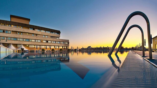 Un hotel moderno con piscina, un edificio amplio con muchas ventanas y vistas al atardecer.