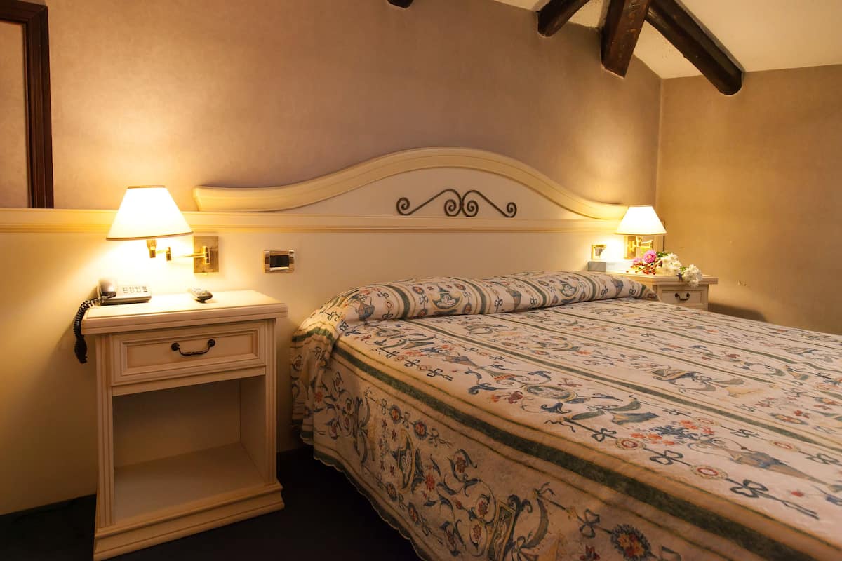 A hotel room with a bed, two bedside tables with lamps, a nightstand, and a wall-mounted telephone.