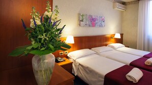 Une chambre d’hôtel avec deux lits, une tête de lit en bois, une table de chevet avec un téléphone, un vase avec des fleurs et un tableau au mur.