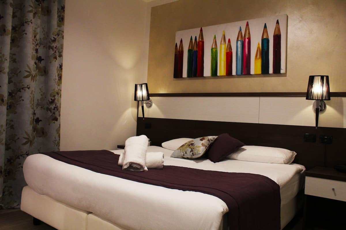 Ein Hotelzimmer mit einem großen Bett, zwei Nachttischlampen, einem blumigen Vorhang und einem farbenfrohen Bild an der Wand.