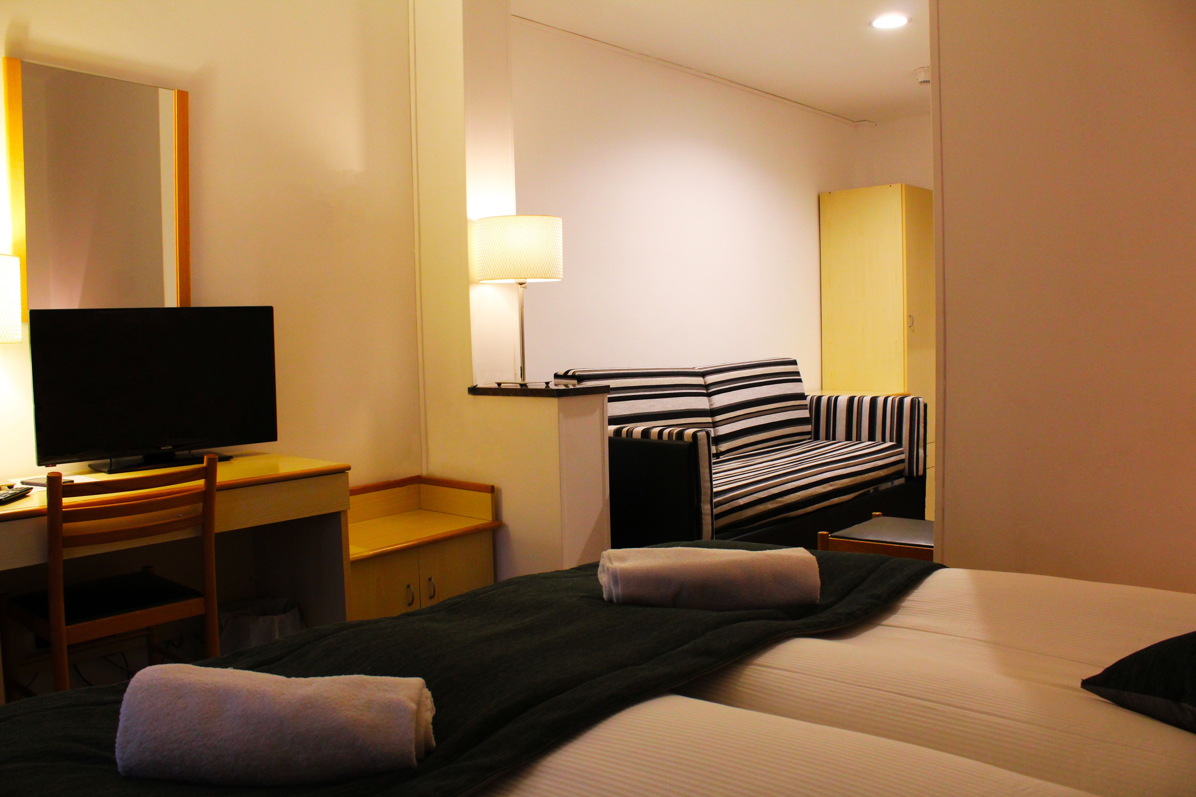 A hotel room with two beds, a desk, a television, and a lamp.