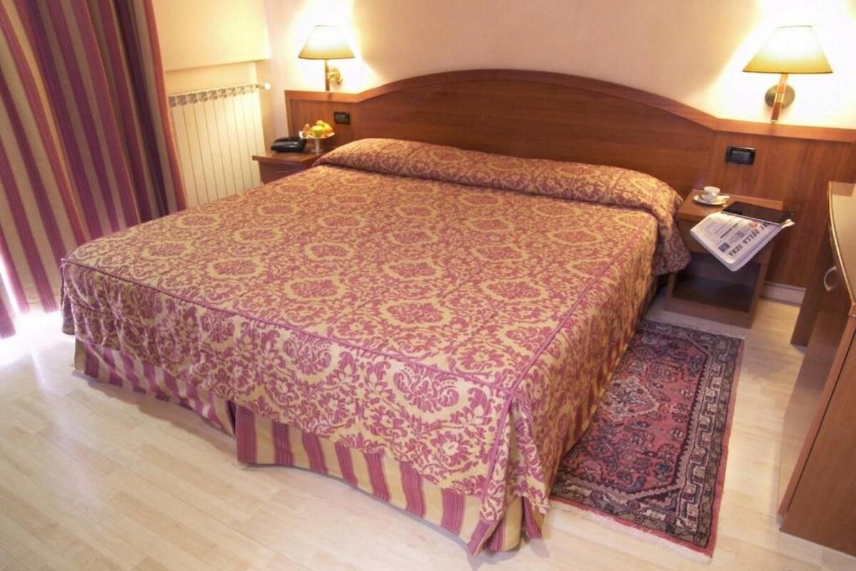 A hotel room with a large bed, two bedside lamps, a nightstand, and a rug.