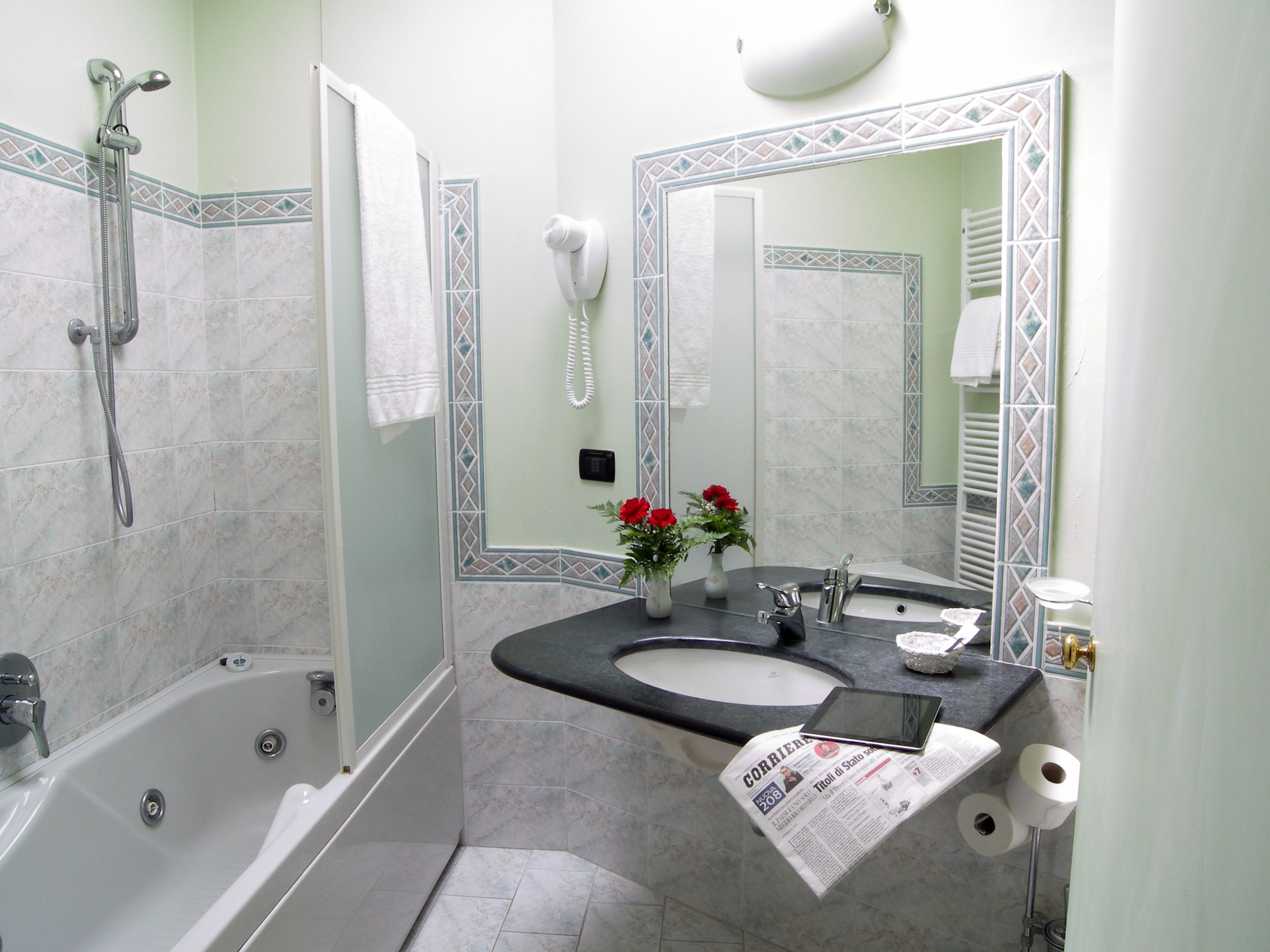 A bathroom with a bathtub, a sink, a mirror, a hairdryer, and a newspaper on the counter.