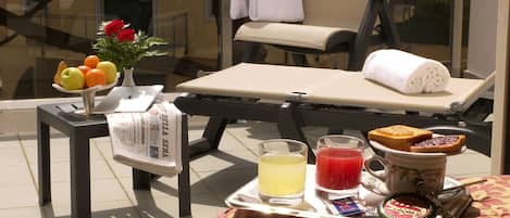 A sun lounger with a towel, a tray with breakfast items, and a newspaper on a table.