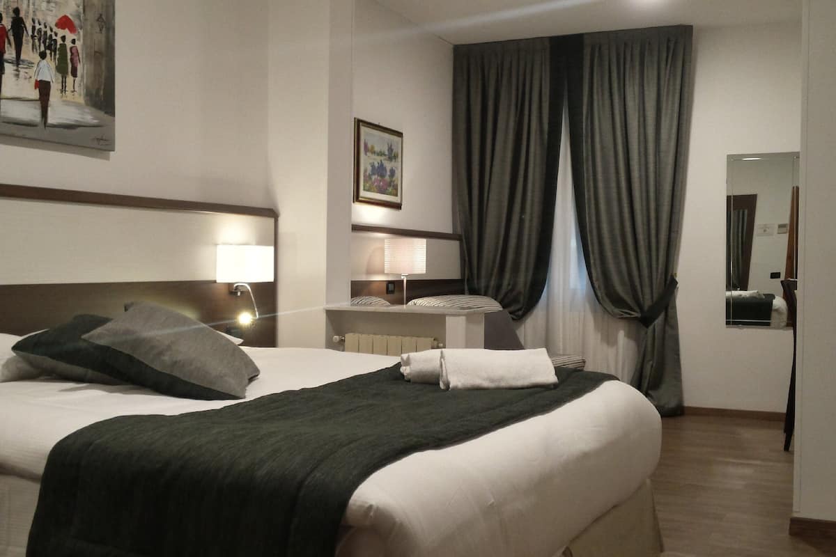 Ein Hotelzimmer mit einem großen Bett, einem Nachttisch mit Lampe, einem Bild an der Wand und einem Fenster mit Vorhängen.