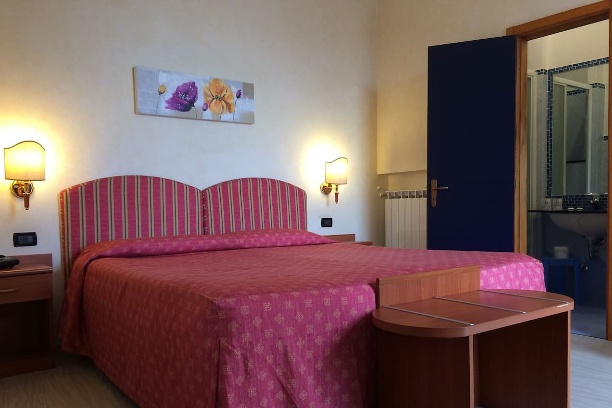 Ein Schlafzimmer mit einem Bett, zwei Nachttischen, einem Wandbild und einer Tür zu einem Badezimmer.