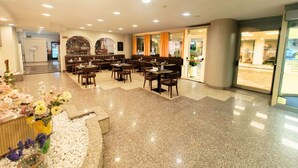 A spacious restaurant with multiple seating areas, a bar, and a view of the street through large windows. - Hotel Pineta Palace (Rome)