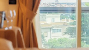 A hotel room with a bed, a window with curtains, and a view of buildings and greenery. - Hotel Pineta Palace (Rome)