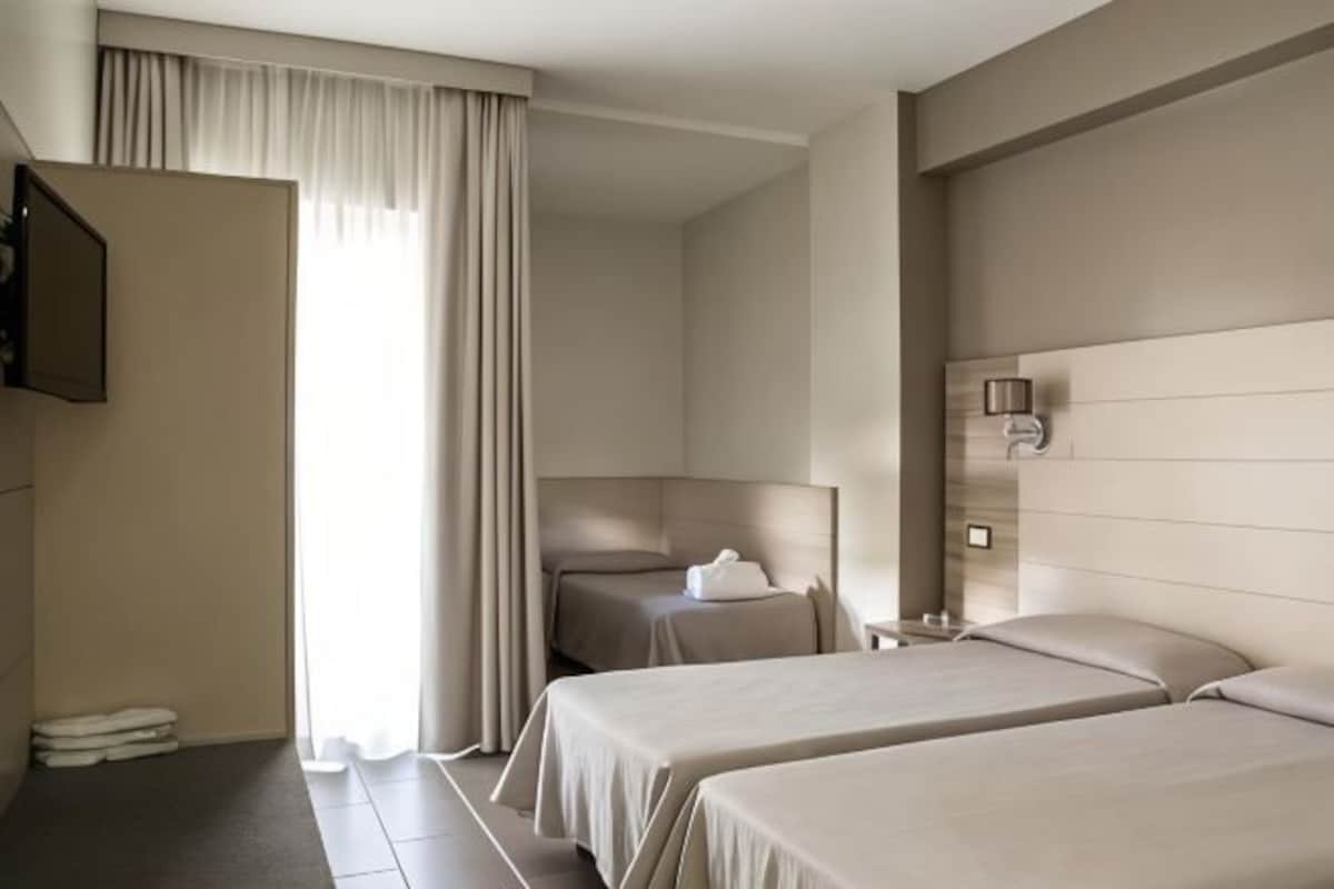 A hotel room with two beds, a desk, a chair, a TV, and a window with curtains.