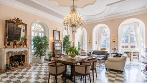 Un salón amplio con suelo a cuadros, una araña y una chimenea decorada con figuritas.